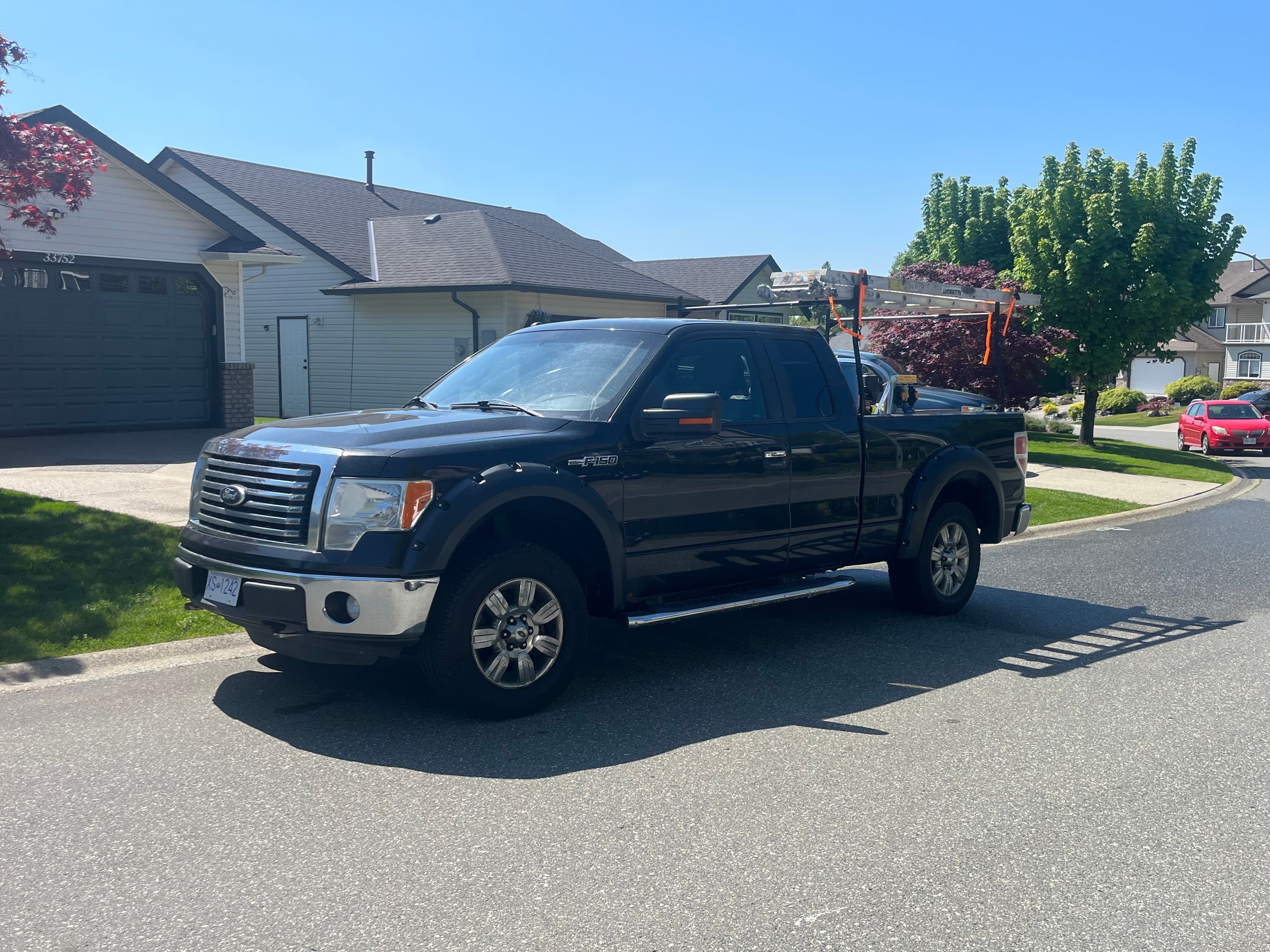 Black Ford F-150 pickup truck with a ladder rack parked on a suburban street.